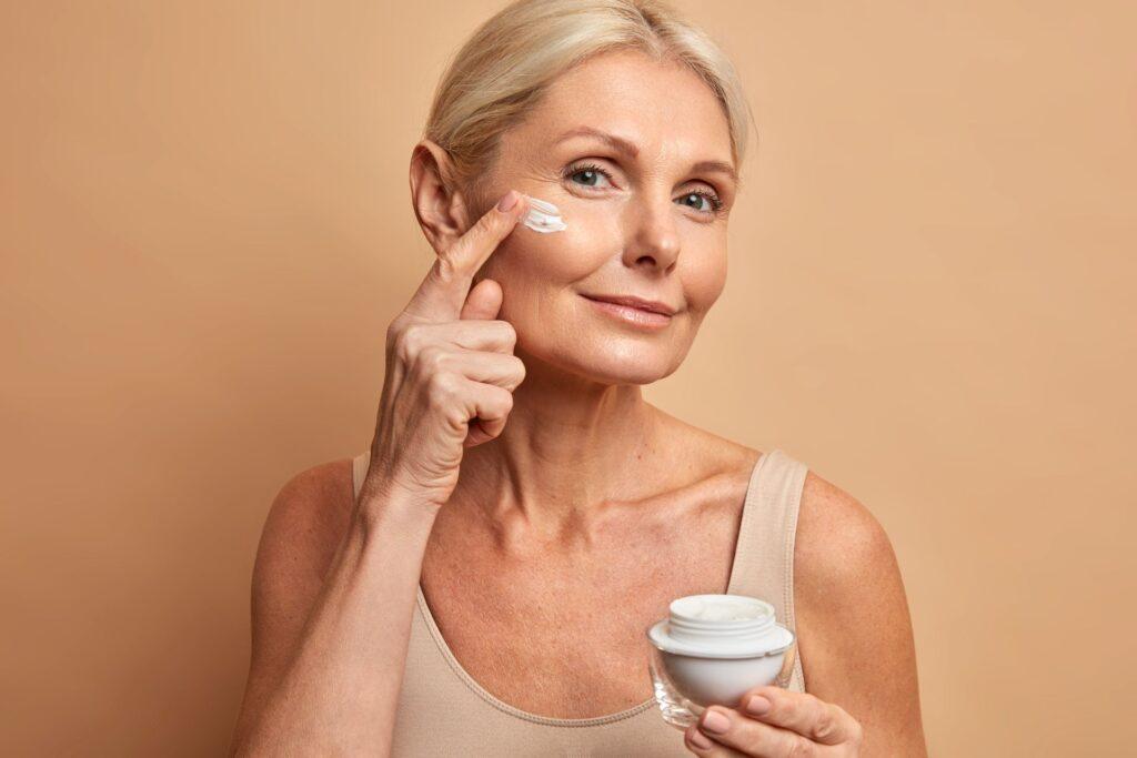 Reife Frau trägt eine hochwertige Anti-Aging-Creme auf ihre Haut auf – eine perfekte Pflegeoption, die in Ihrer Online Drogerie verfügbar ist.