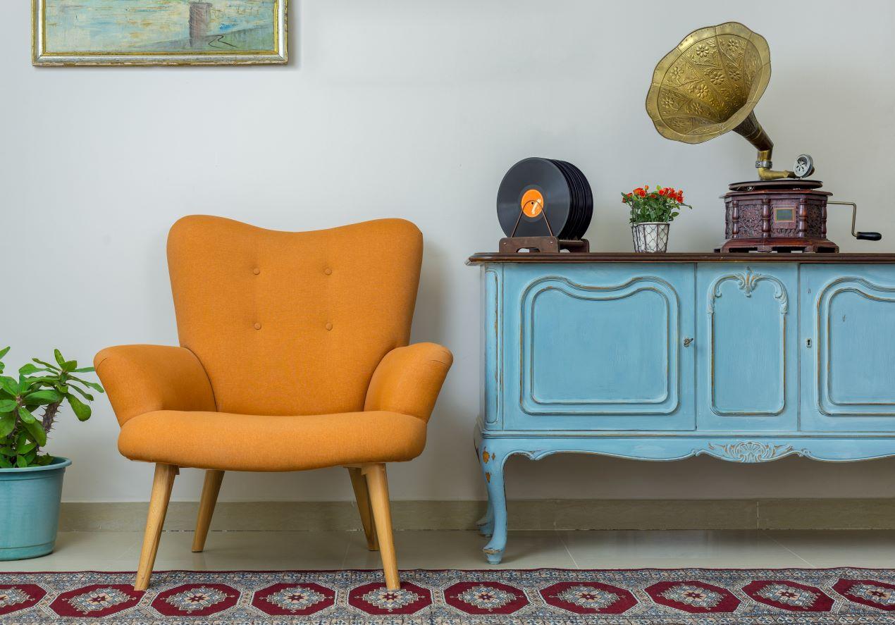 Blaues Vintage-Sideboard mit kunstvollen Verzierungen, kombiniert mit einem orangefarbenen Sessel und einem nostalgischen Grammophon.