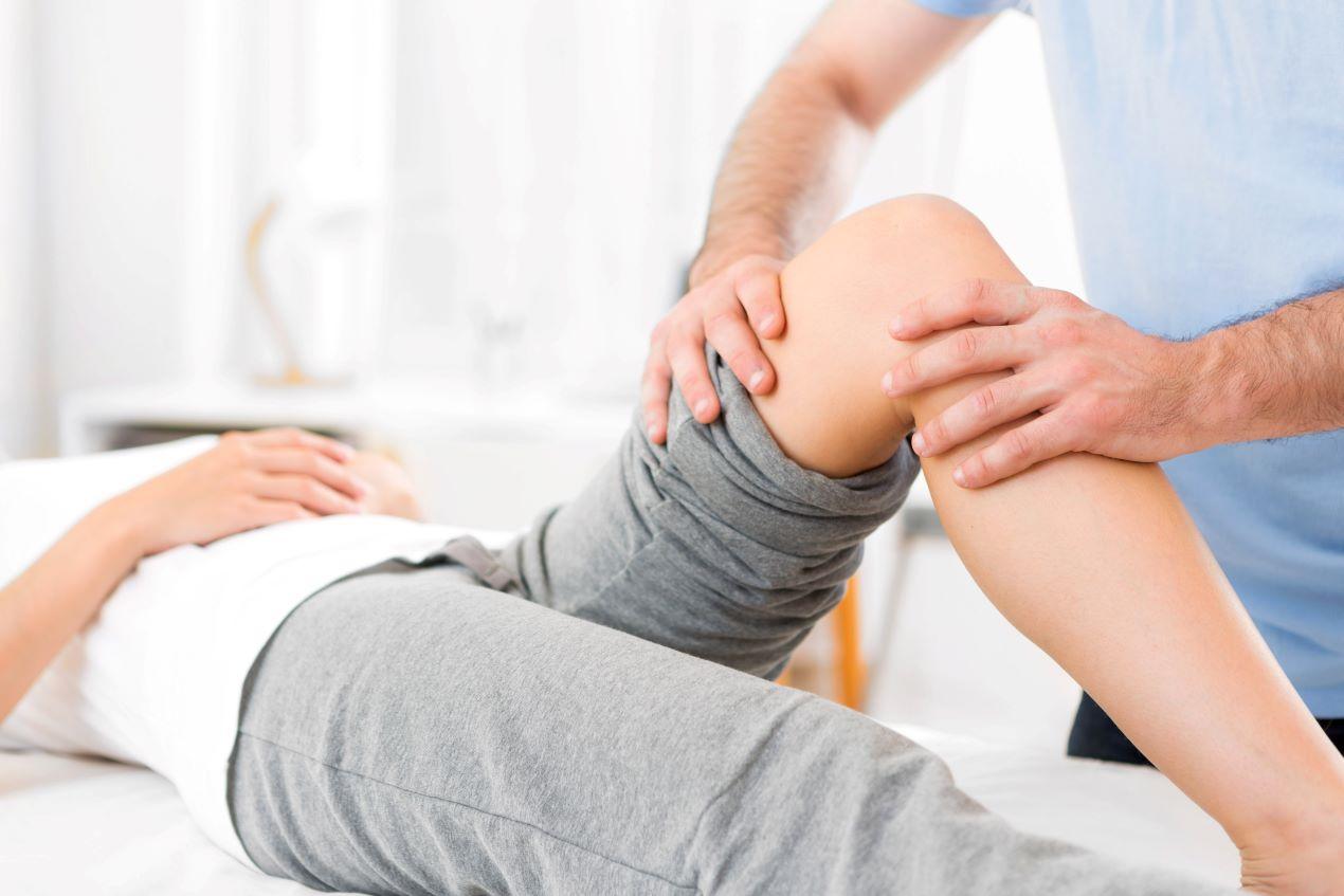 Ein Orthopäde in Köln untersucht das Knie einer Patientin und führt eine physiotherapeutische Behandlung durch.