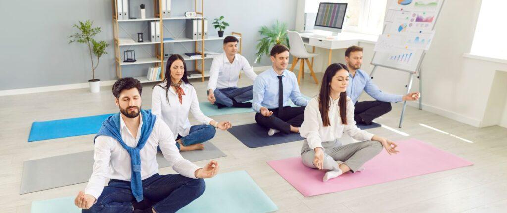 Mitarbeitende in Business-Kleidung meditieren auf Yogamatten im Buero – ein Zeichen fuer erfolgreiche Mitarbeiterberatung zur Stressbewaeltigung.