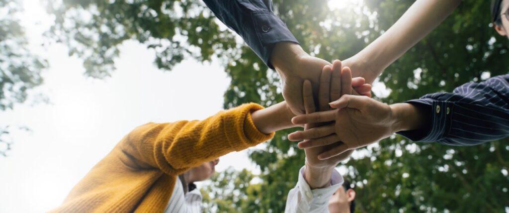 Mehrere Menschen legen ihre Haende aufeinander – Symbolbild fuer Zusammenhalt, Teamgeist und Werte einer Hilfsorganisation Schweiz