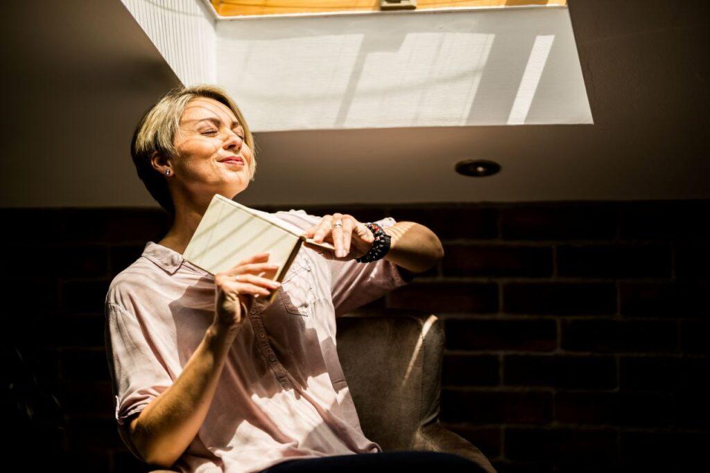 Zufriedene Frau sitzt im Sonnenlicht mit Buch – Darstellung der positiven Wirkung von sozialem Engagement bei Hilfsorganisation Schweiz