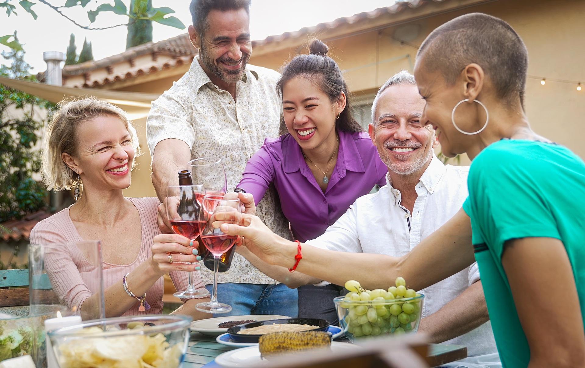 Freunde stoßen am Tisch im Garten mit Wein an | Outdoor Küche